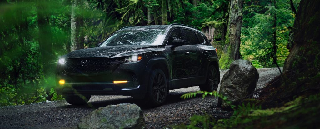 A black Mazda SUV driving through a misty forest trail