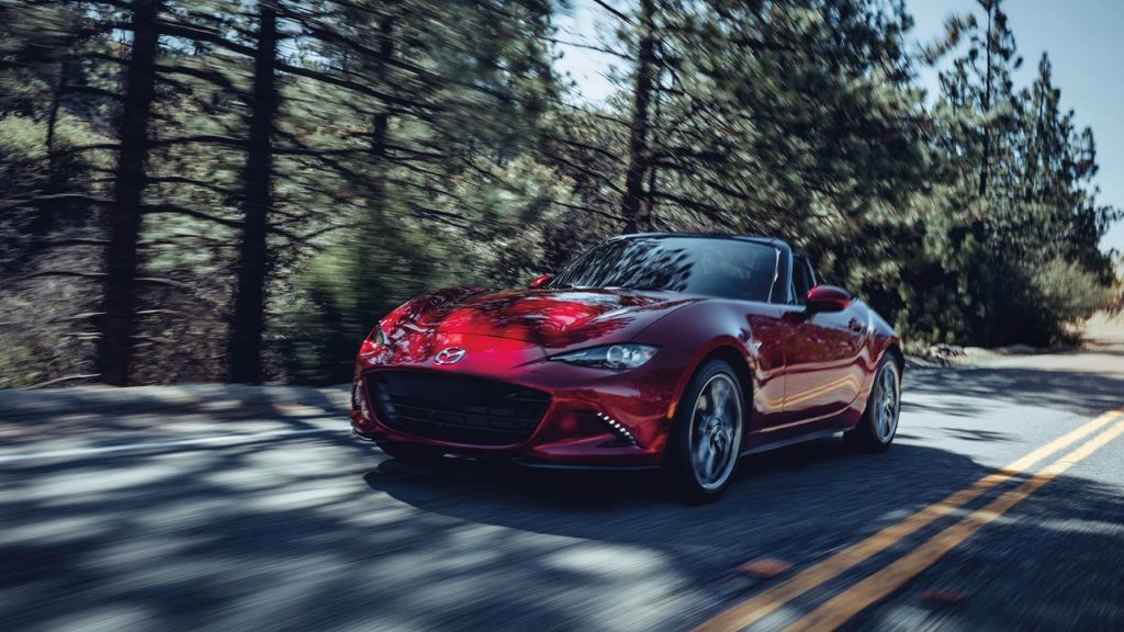 Mazda MX-5 Miata driving on winding road, red convertible