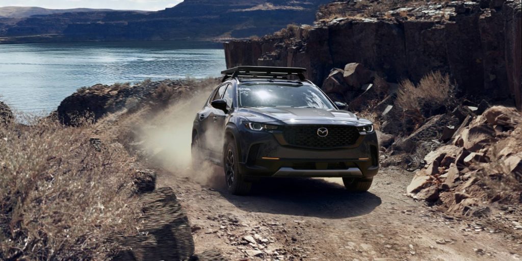 Dark Mazda CX-50 driving on a rugged trail near a rocky coastline.