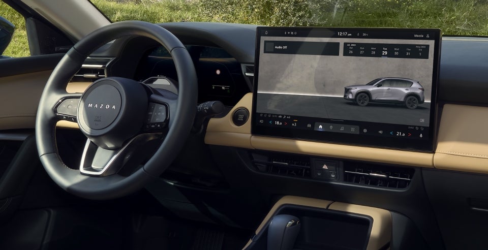 Mazda vehicle interior showing the steering wheel, dashboard, and large infotainment touchscreen display.